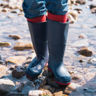 Classic Wellies Navy: A person wearing navy wellies and red socks stands in a rocky stream, their blue jeans cuffs visible above the boot tops.